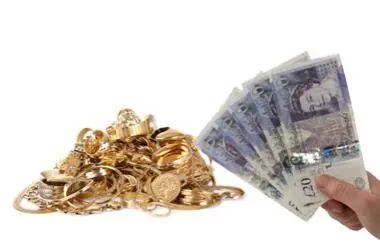 A pile of scrap gold jewellery beside a hand holding twenty pound notes